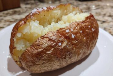 A perfectly cooked air fryer baked potato, split open to show fluffy insides and a crispy, salted skin.