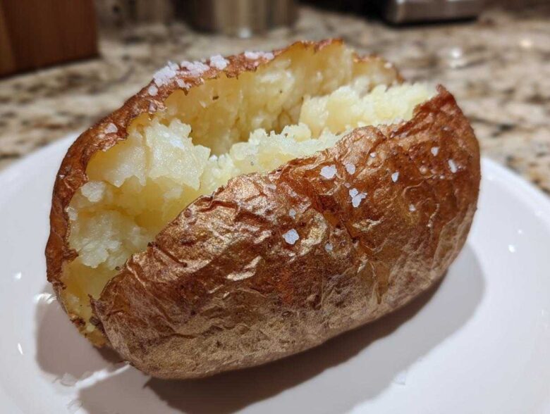 A perfectly cooked air fryer baked potato, split open to show fluffy insides and a crispy, salted skin.