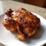 A perfectly cooked, glistening air fryer whole chicken with crispy, seasoned skin resting on a white plate.