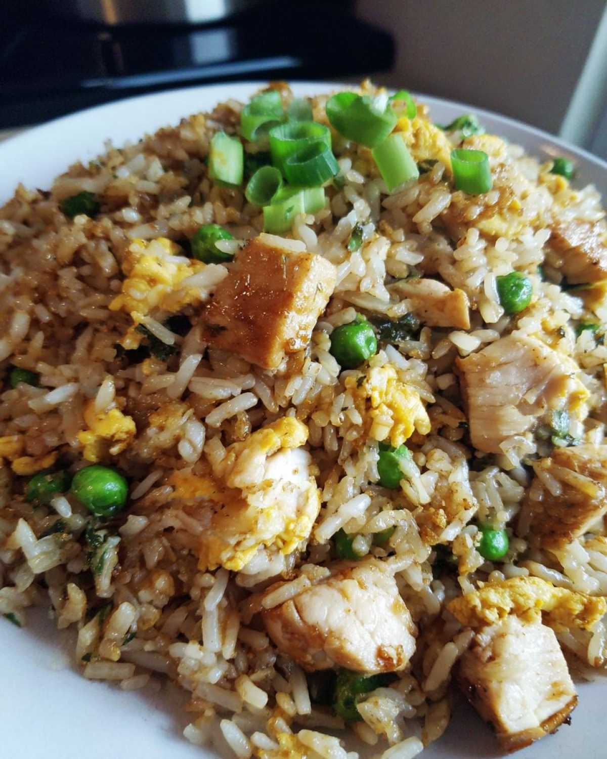 A close-up serving of homemade chicken fried rice featuring chunks of chicken, scrambled egg, peas, and green onions.