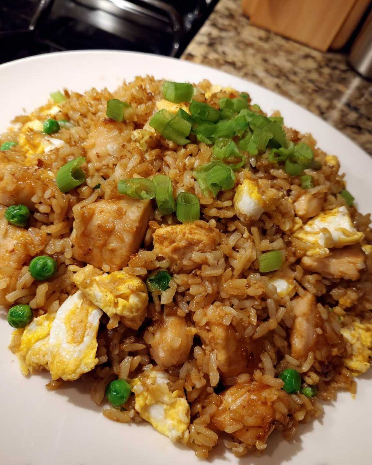 A close-up of a generous serving of chicken fried rice, featuring chunks of chicken, scrambled egg, peas, and green onion garnish.