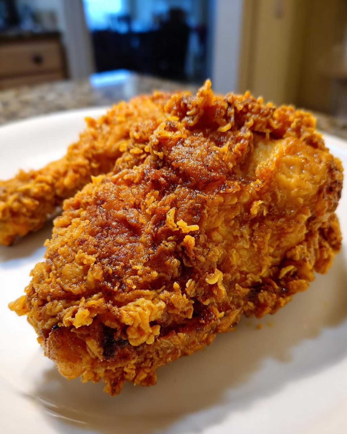 A close-up shot of a perfectly golden brown, crispy piece of fried chicken resting on a white plate.