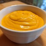 A close-up of thick, vibrant orange homemade nacho cheese sauce served in a small white bowl.
