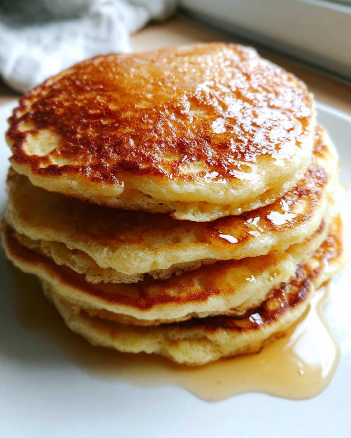 Close-up of a tall stack of fluffy almond flour pancakes drizzled with syrup.