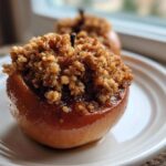 A close-up of a glistening, caramelized baked apple topped generously with a brown sugar and oat crumble.