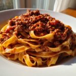 Close-up of rich, meaty bolognese sauce generously spooned over a nest of fresh tagliatelle pasta.