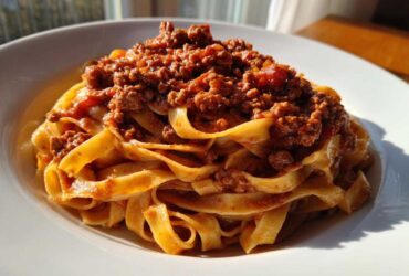 Close-up of rich, meaty bolognese sauce generously spooned over a nest of fresh tagliatelle pasta.