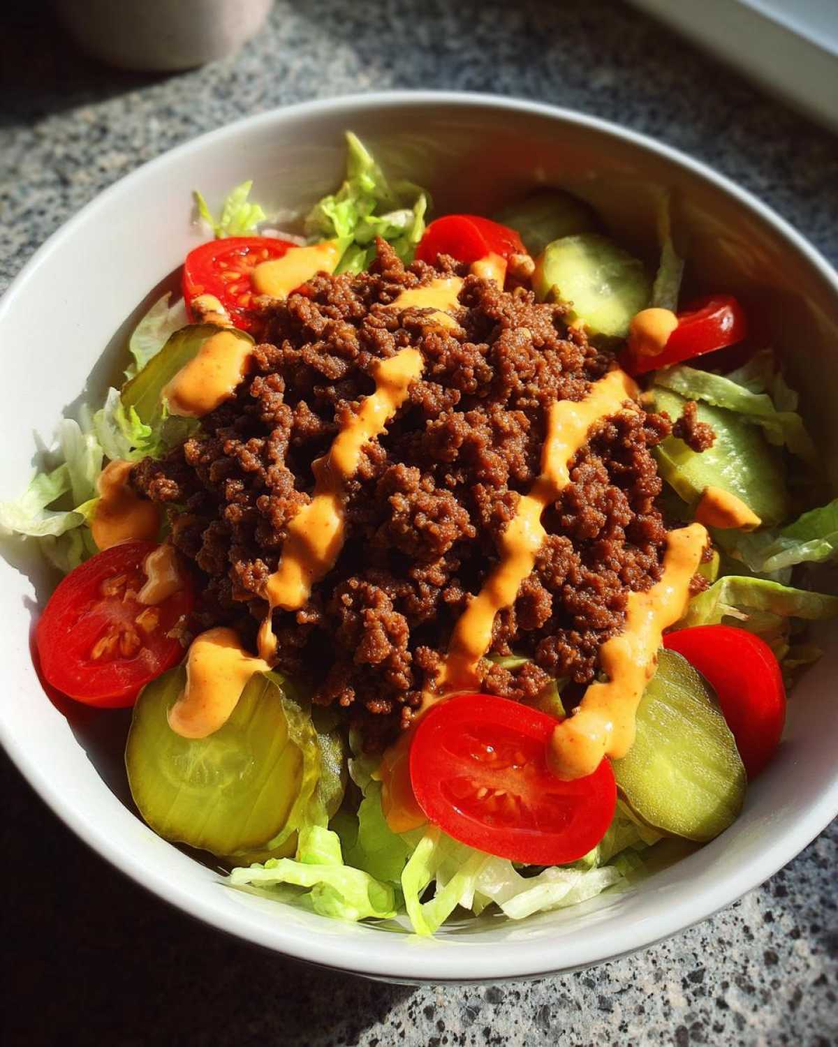 A close-up of a fresh cheeseburger bowl featuring seasoned ground beef, lettuce, tomato, pickles, and special sauce.