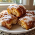 Close-up of gooey, glazed cinnamon roll bites piled on a small white plate, ready to eat.