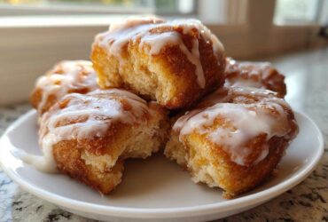 Close-up of gooey, glazed cinnamon roll bites piled on a small white plate, ready to eat.