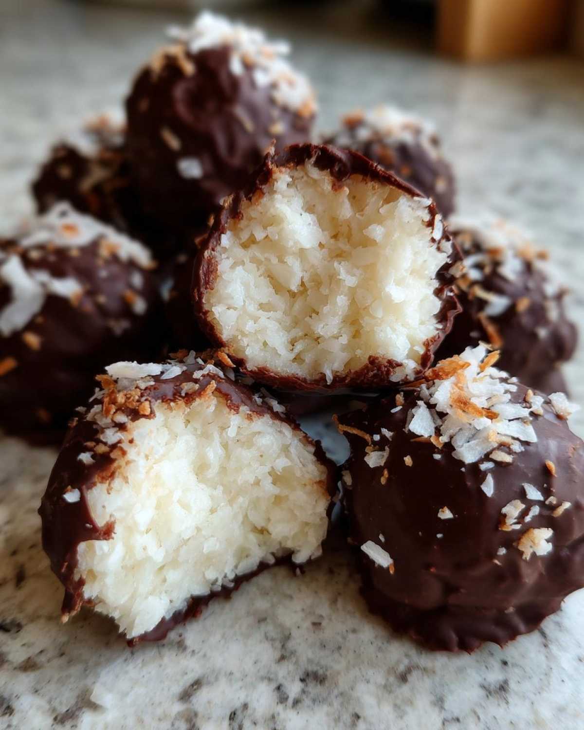 Close-up of several chocolate-dipped coconut balls, one cut open to show the shredded coconut filling.