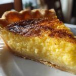 Close-up of a rich, yellow slice of egg custard pie with a browned, cinnamon-dusted top.