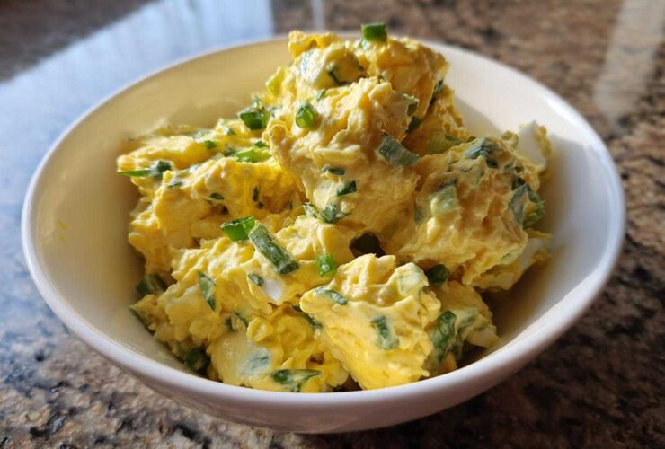 Close-up of creamy, yellow egg salad recipe garnished with chopped green onions in a white bowl.