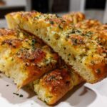 Close-up of fluffy, golden brown breadsticks cut open, topped with melted cheese, garlic butter, and fresh parsley.