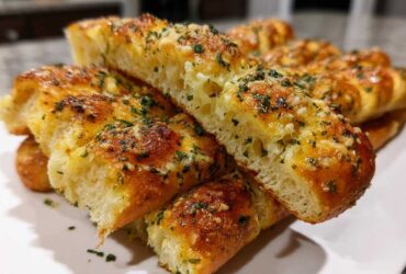 Close-up of fluffy, golden brown breadsticks cut open, topped with melted cheese, garlic butter, and fresh parsley.
