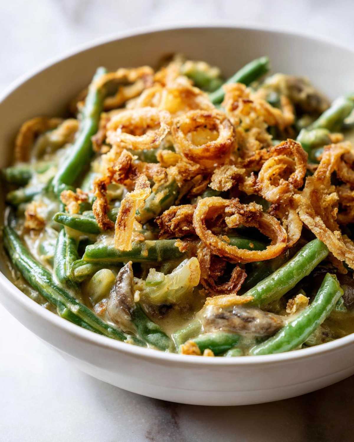 A close-up shot of a white bowl filled with creamy green bean casserole topped generously with crispy fried onions.