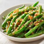 Close-up of vibrant, cooked green beans topped with crispy brown bits and grated cheese.