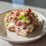 A scoop of creamy ham salad with diced ham, celery, and crispy topping on a speckled white plate.
