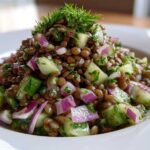Close-up of a vibrant lentil salad featuring brown lentils, diced cucumber, red onion, and fresh dill garnish.