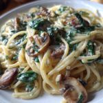 Close-up of a serving of creamy mushroom pasta with spinach, featuring spaghetti coated in a rich sauce.