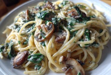 Close-up of a serving of creamy mushroom pasta with spinach, featuring spaghetti coated in a rich sauce.
