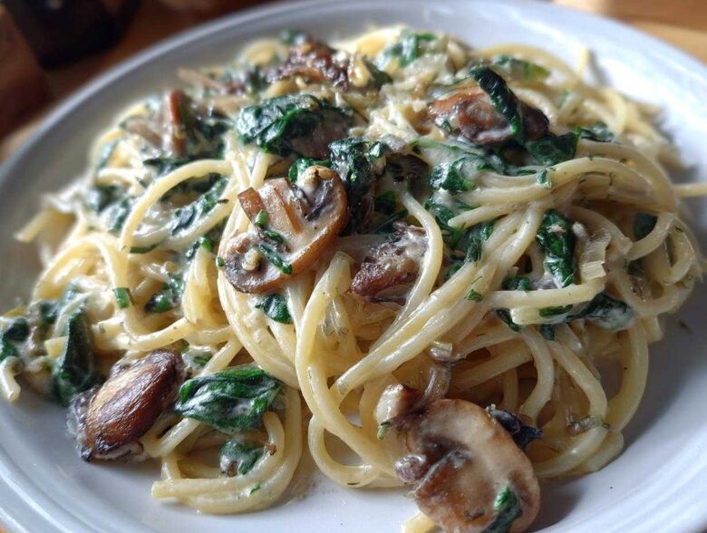 Close-up of a serving of creamy mushroom pasta with spinach, featuring spaghetti coated in a rich sauce.