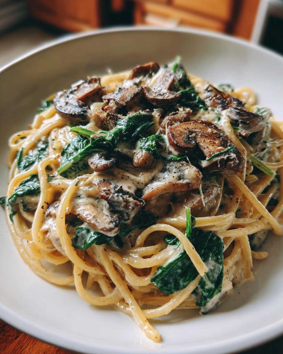 Close-up of creamy mushroom pasta tossed with wilted spinach and topped with sliced mushrooms and black pepper.