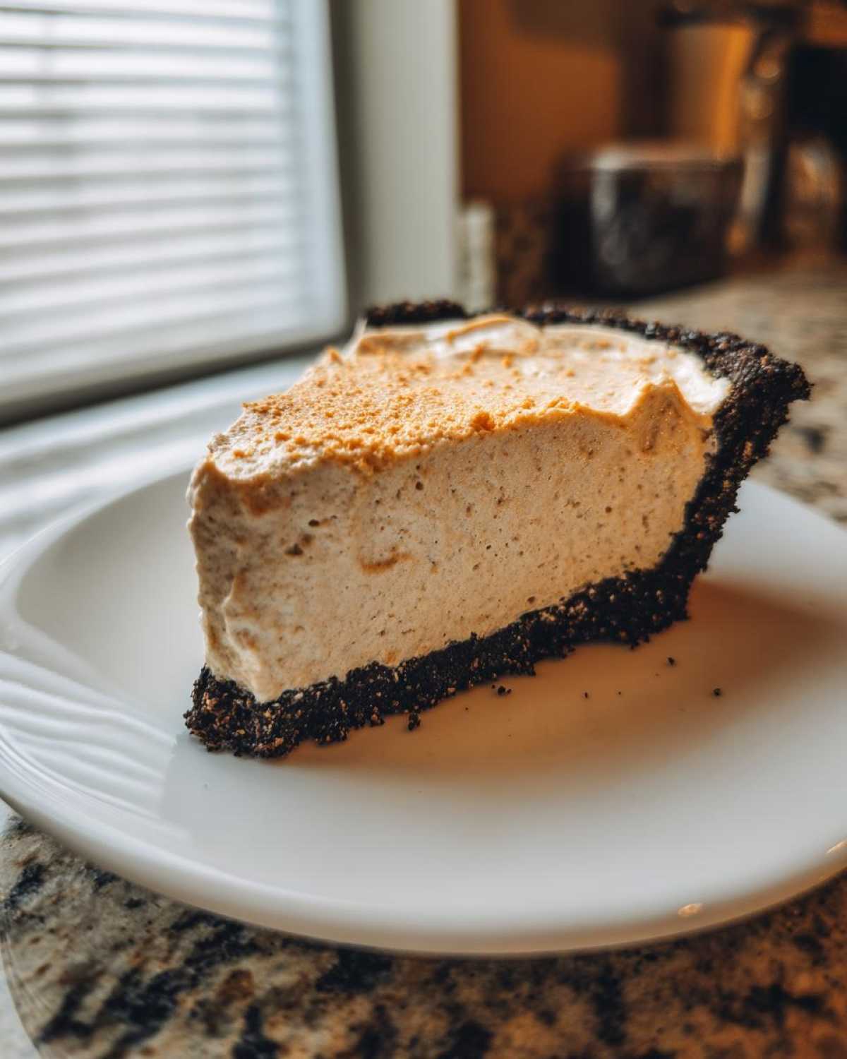 A thick slice of creamy peanut butter pie with a dark chocolate crust served on a white plate.