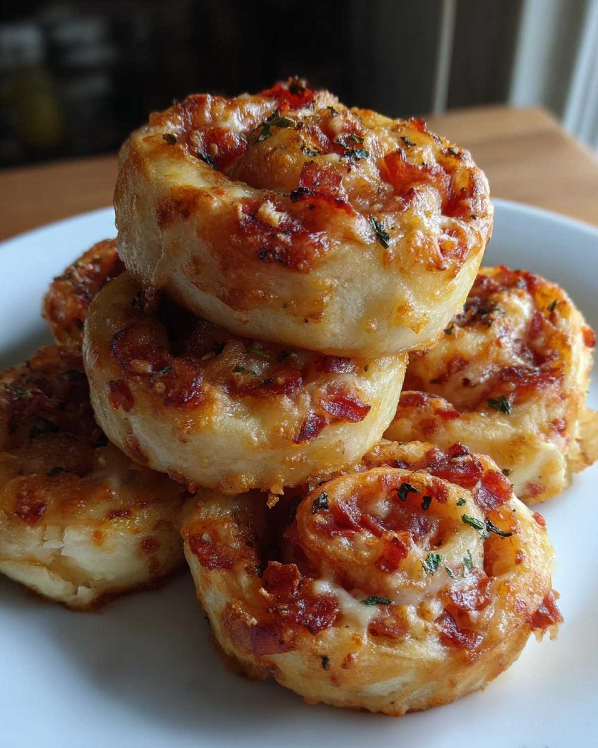 A stack of golden brown, baked pizza pinwheels topped with bacon bits and herbs on a white plate.