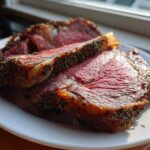 Slices of medium-rare prime rib roast, crusted with herbs, resting on a white plate.