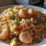A close-up, sunlit view of a plate piled high with amazing shrimp fried rice, featuring plump shrimp, scrambled egg, carrots, and green onions.