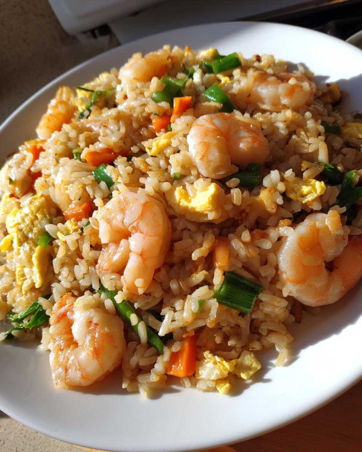 Close-up of a white plate piled high with flavorful shrimp fried rice, featuring large shrimp, scrambled egg, and diced carrots.