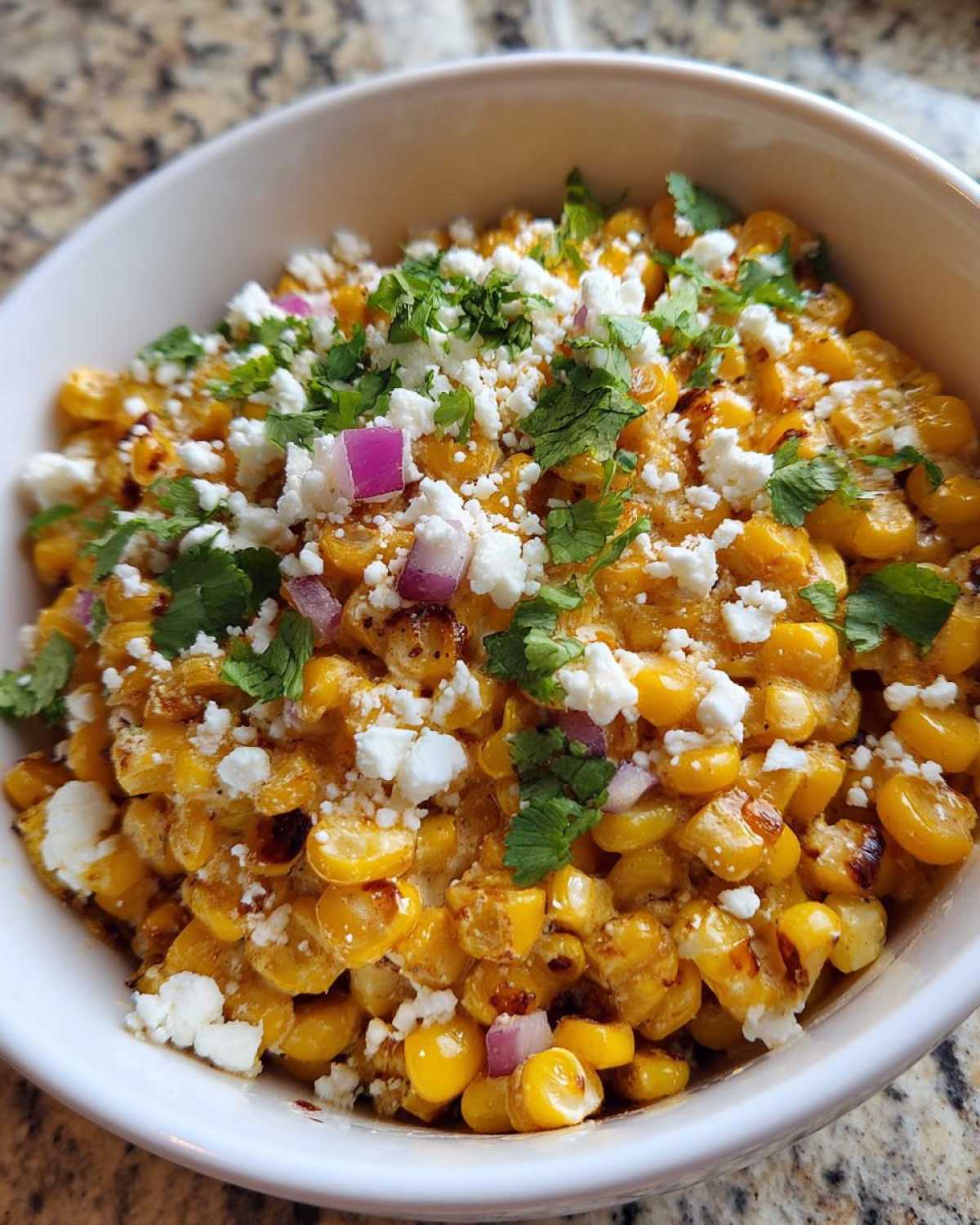 Close-up of a white bowl filled with amazing street corn salad, topped with cotija cheese, red onion, and cilantro.