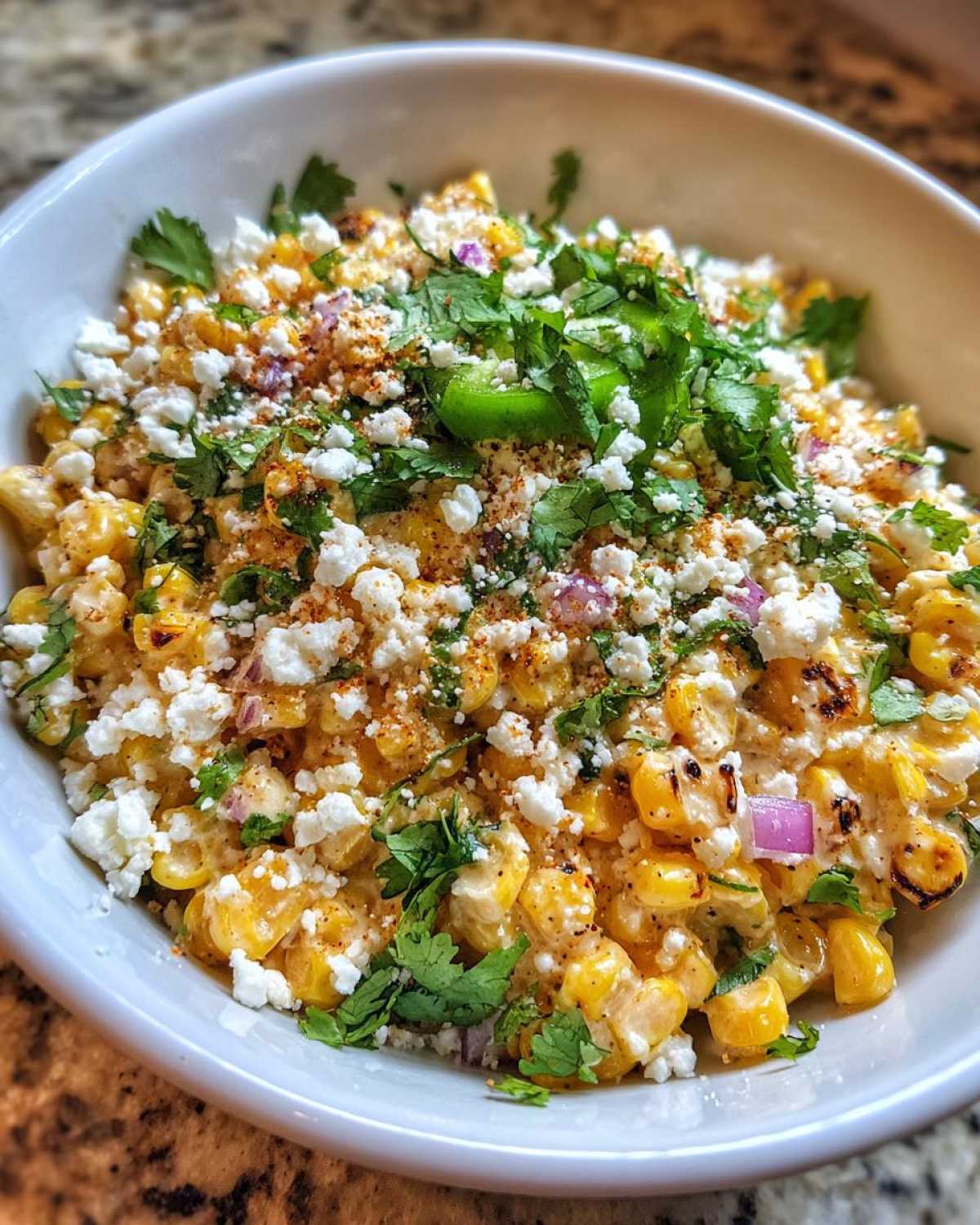 Close-up of creamy, charred corn kernels topped with crumbled white cheese, cilantro, and red onion, showcasing the amazing street corn salad.