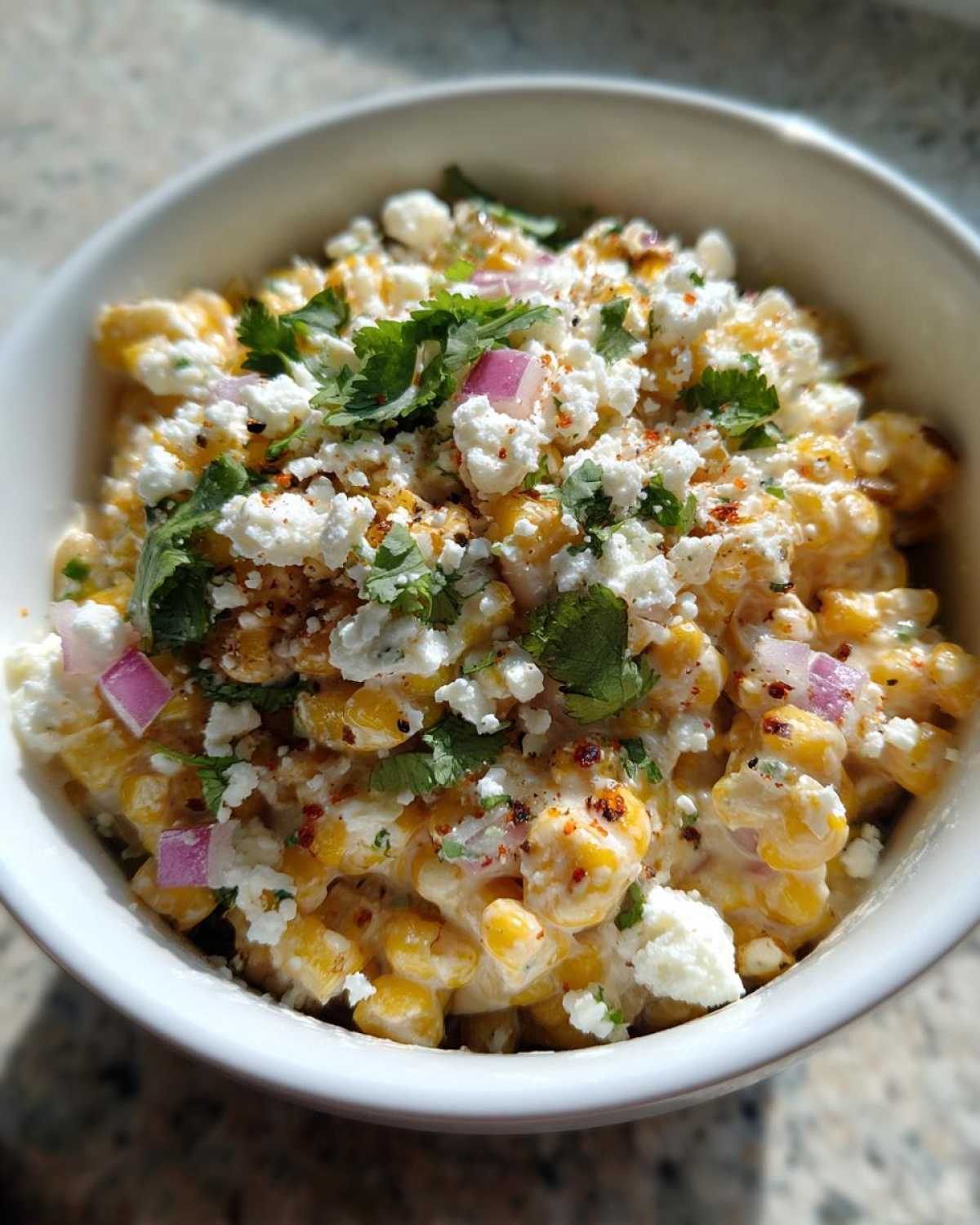 Close-up of creamy, vibrant street corn salad topped with cotija cheese, cilantro, and red onion.
