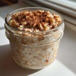 Close-up of apple cinnamon overnight oats prepared in a glass jar, topped with diced apples and cinnamon.
