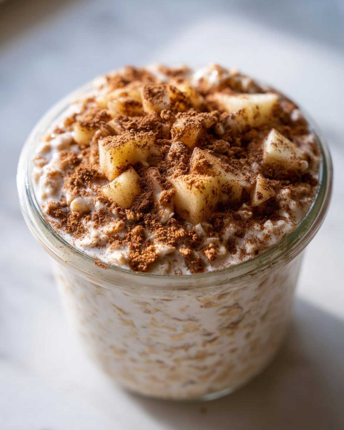 Close-up of creamy apple cinnamon overnight oats topped with diced apples and a generous dusting of cinnamon.