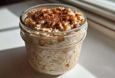 Close-up of apple cinnamon overnight oats prepared in a glass jar, topped with diced apples and cinnamon.