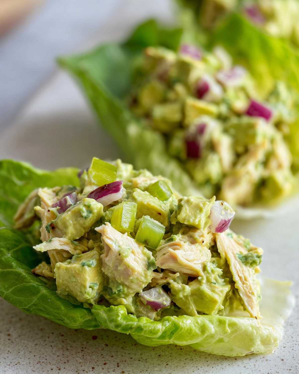 Close-up of creamy avocado chicken salad mixed with red onion and celery served in bright green lettuce cups.