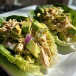 Two lettuce cups filled with creamy avocado chicken salad, featuring chunks of avocado and red onion.