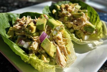 Two lettuce cups filled with creamy avocado chicken salad, featuring chunks of avocado and red onion.