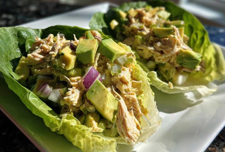 Two lettuce cups filled with creamy avocado chicken salad, featuring chunks of avocado and red onion.
