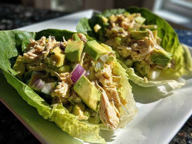 Two lettuce cups filled with creamy avocado chicken salad, featuring chunks of avocado and red onion.