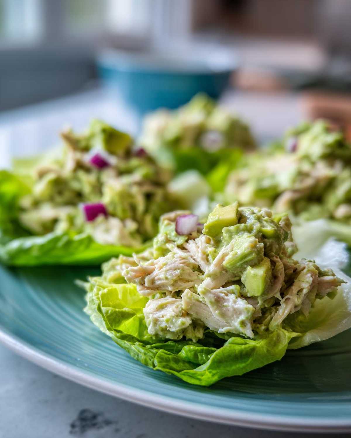 Close-up of creamy avocado chicken salad served in crisp lettuce cups on a teal plate.