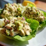 Close-up of creamy avocado chicken salad served in crisp lettuce cups, garnished with red onion.