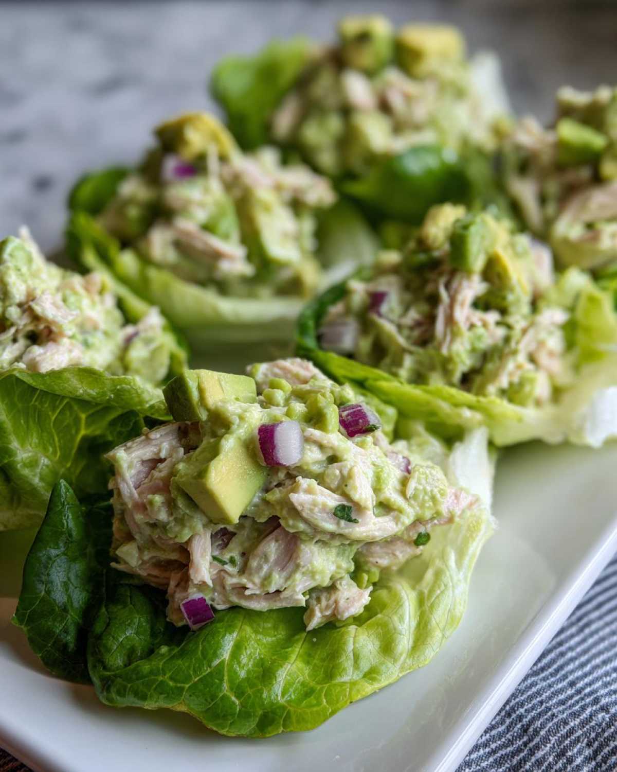 Close-up of fresh avocado chicken salad served in crisp lettuce cups, topped with diced avocado and red onion.