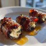 Three bacon wrapped stuffed dates filled with cheese, glistening with a glaze on a white plate.