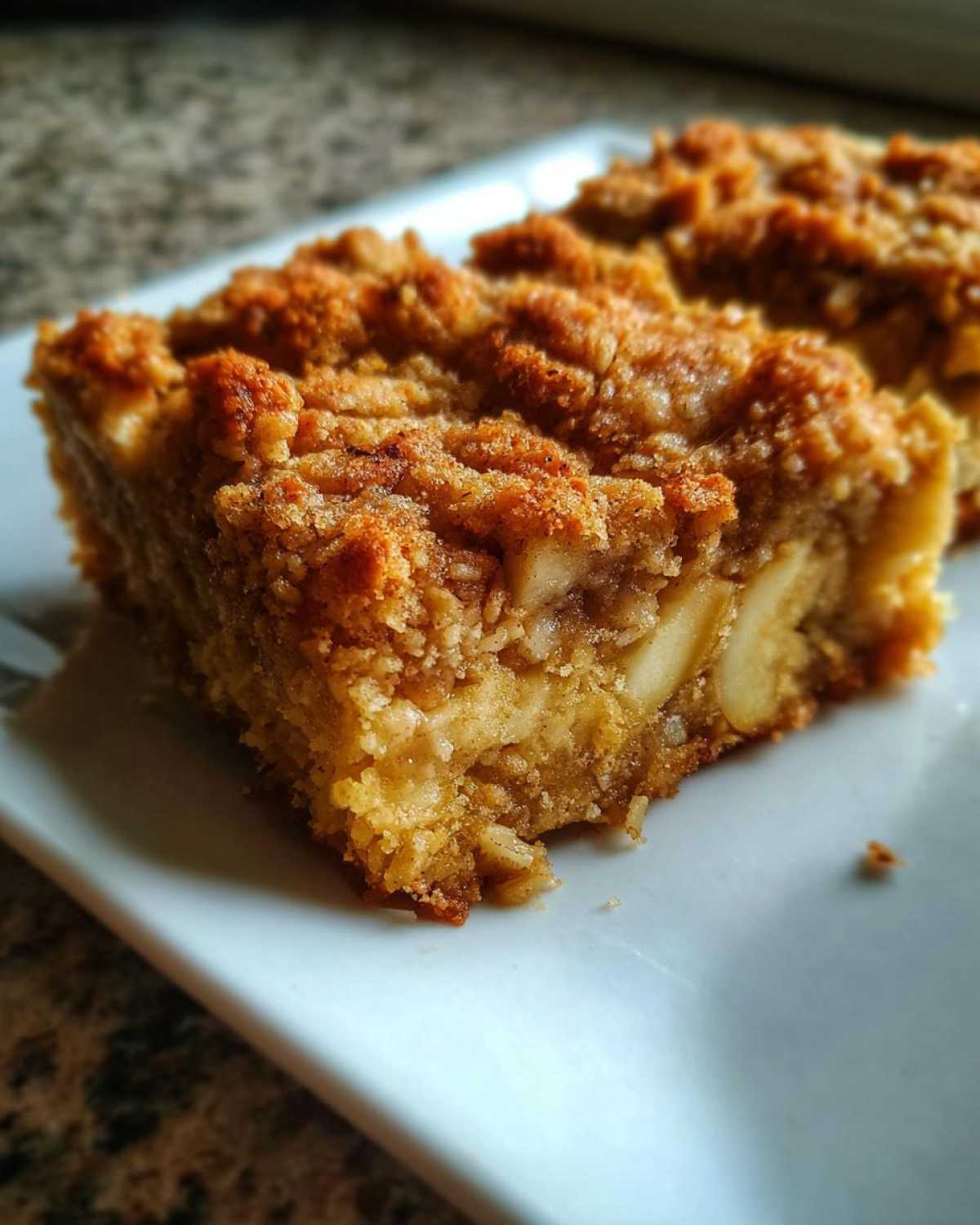 A close-up of a square slice of baked oatmeal with a thick, golden-brown streusel crumb topping.