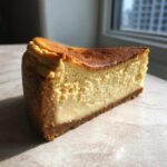 A thick, creamy slice of baked Protein Cheesecake showing a rich, golden-brown top crust.