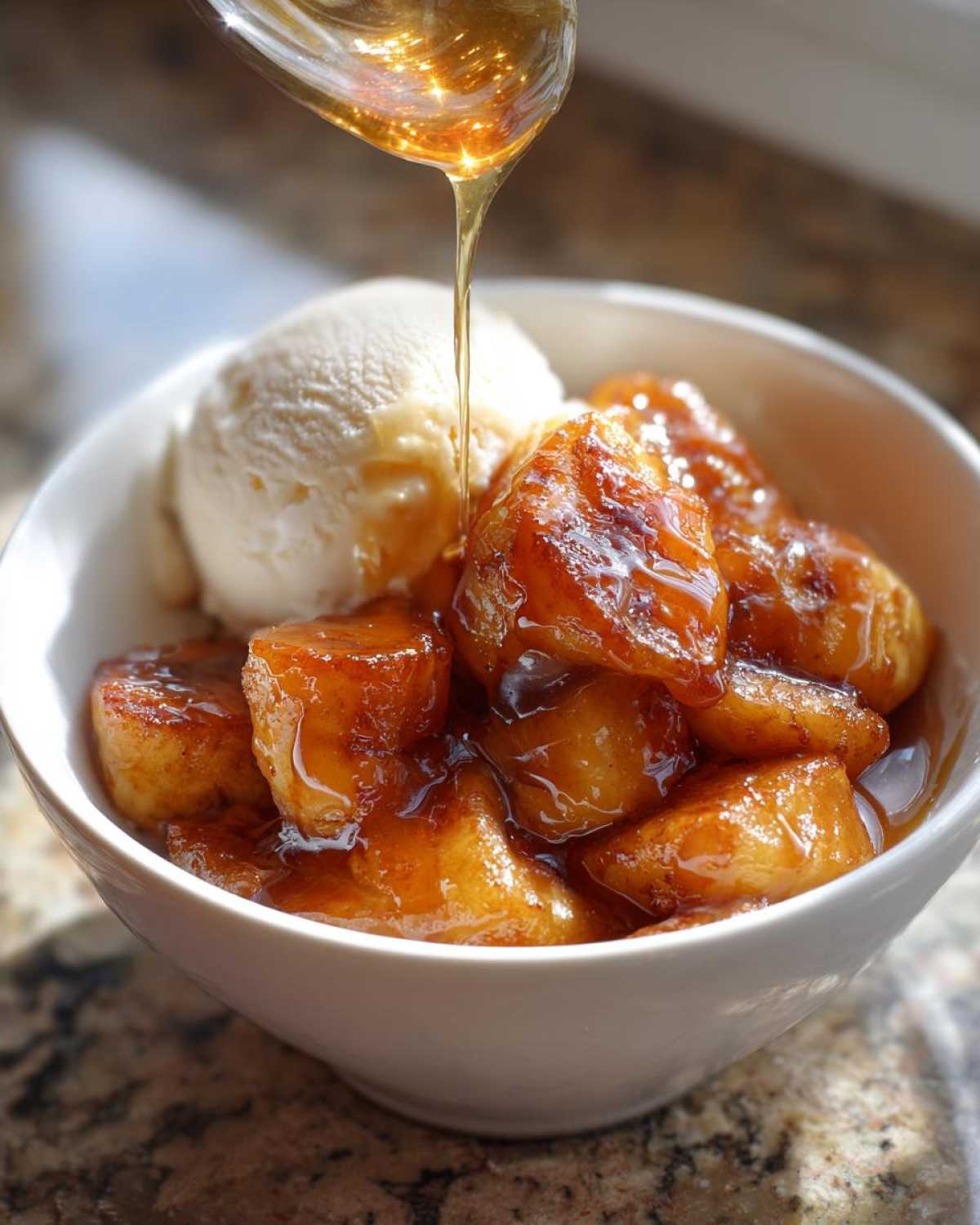 A close-up of caramelized bananas foster being drizzled with warm sauce, served alongside vanilla ice cream in a white bowl.